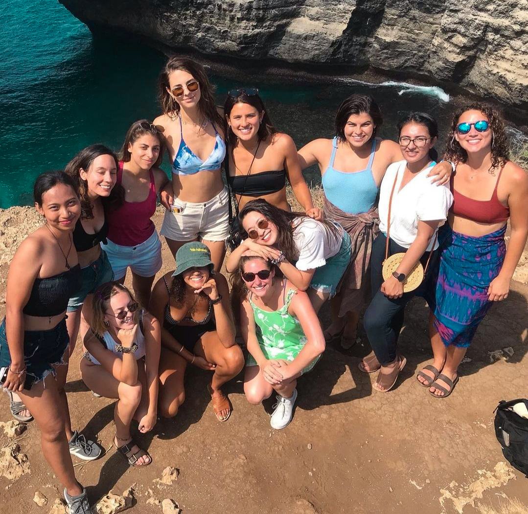 TrovaTrip group of travelers smiling in the sun upwards at a camera above them on an island