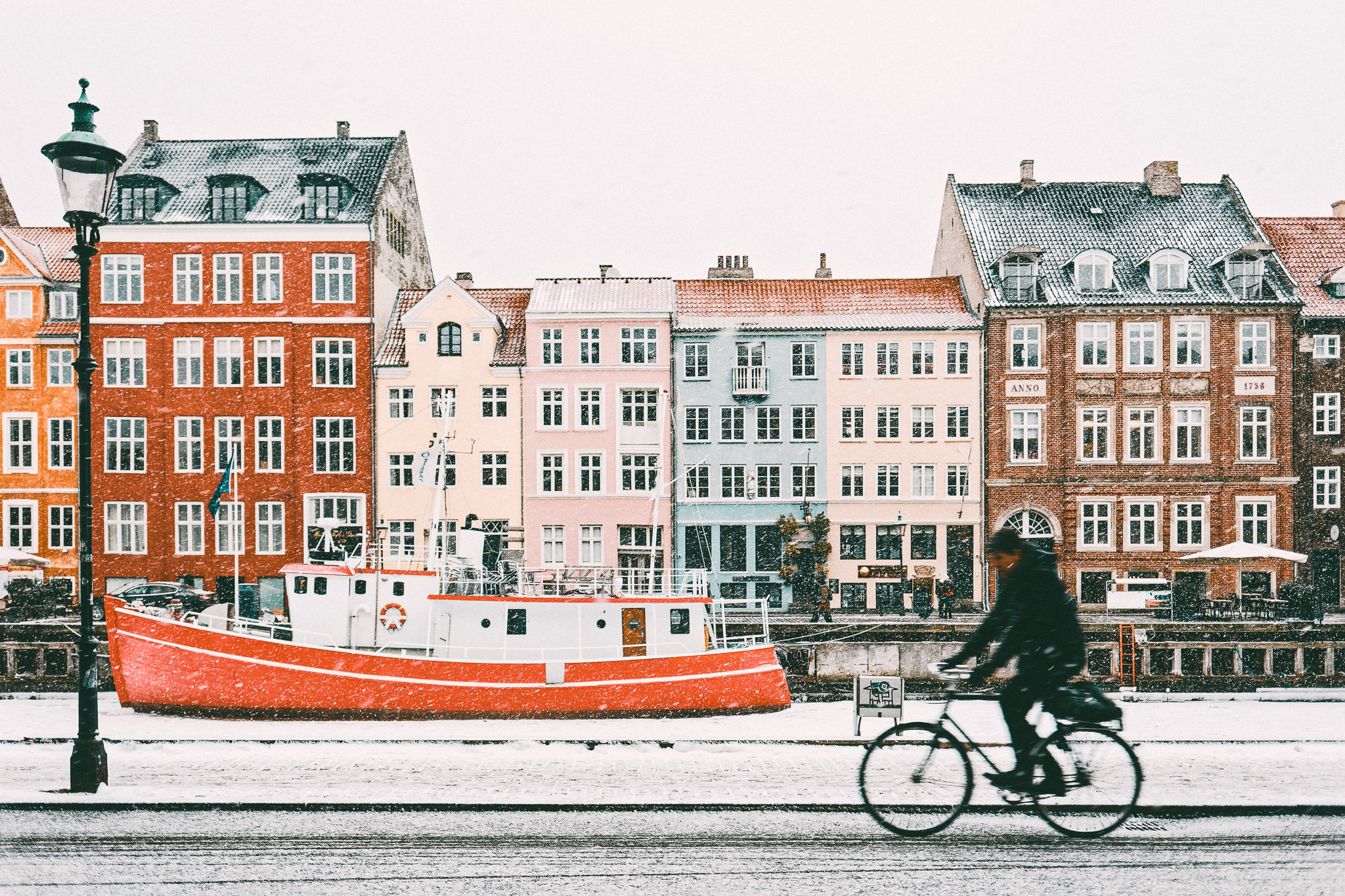 TrovaTrip a person riding a bike down a snowy street with a boat and buildings on the other side of the street in Copenhagen Denmark