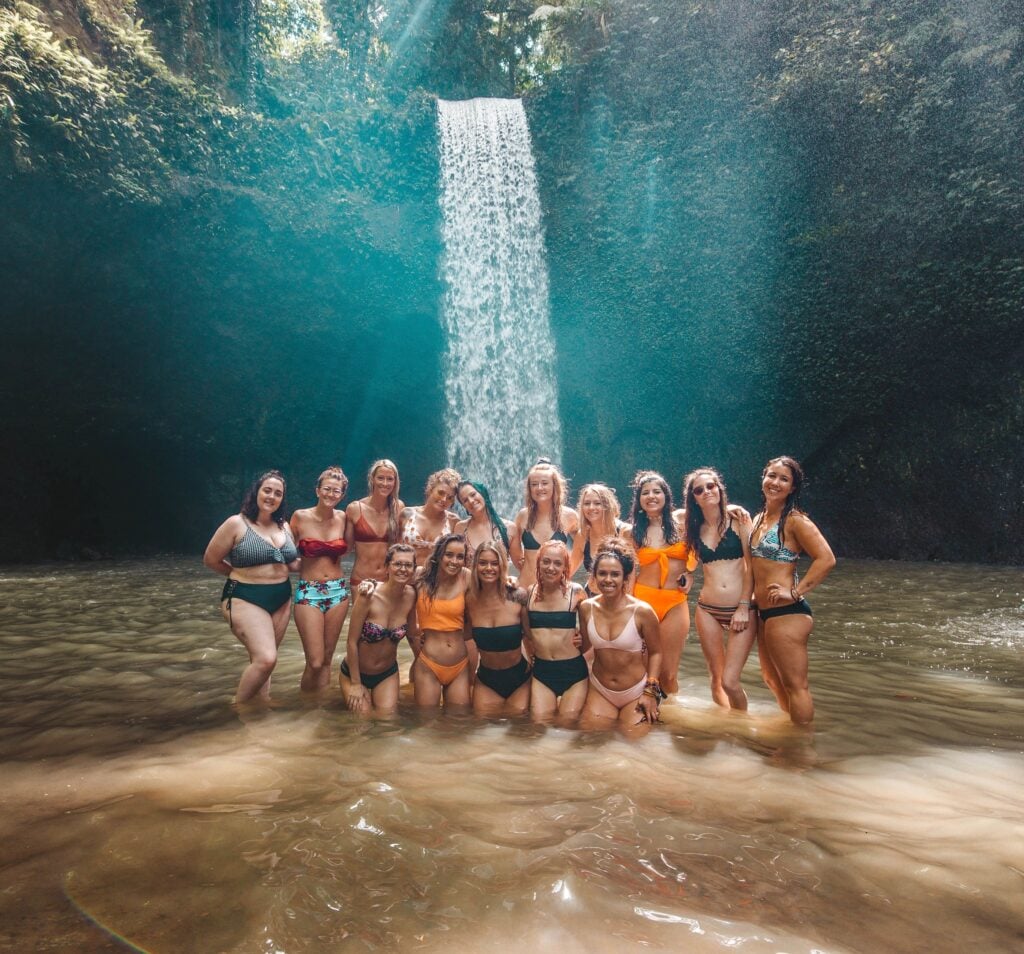 TrovaTrip travelers wearing swimsuits smiling in front of a waterfall