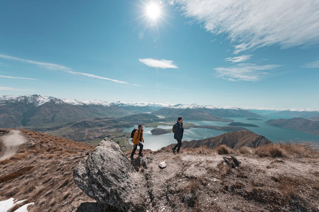 TrovaTrip two travelers hiking on a mountain with lake and snowy mountains behind them