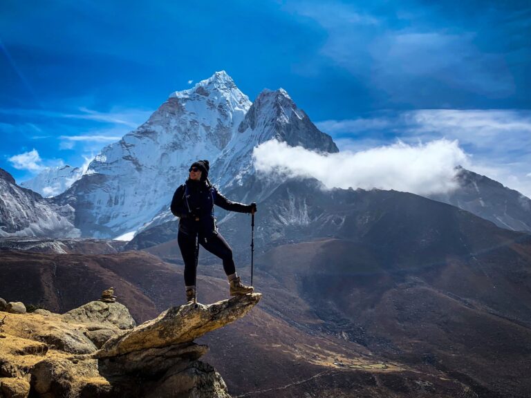 TrovaTrip traveler wearing hiking gear standing on the edge of cliff with snowy mountains behind them