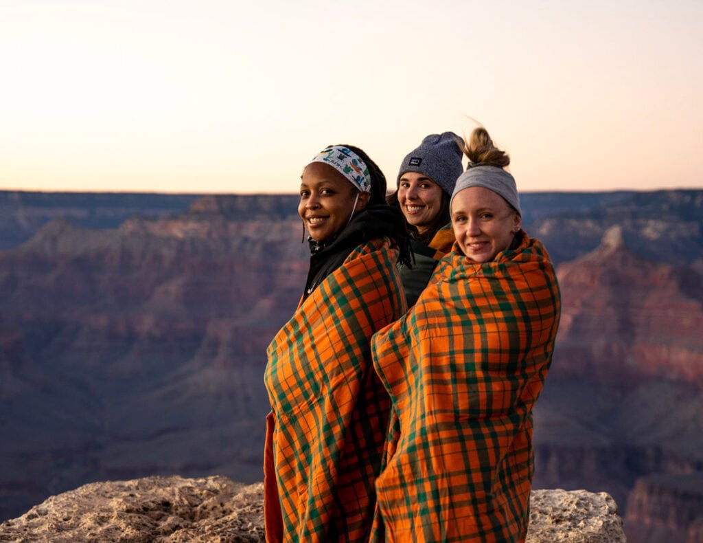 TrovaTrip travelers wearing orange blankets smiling with canyon behind them