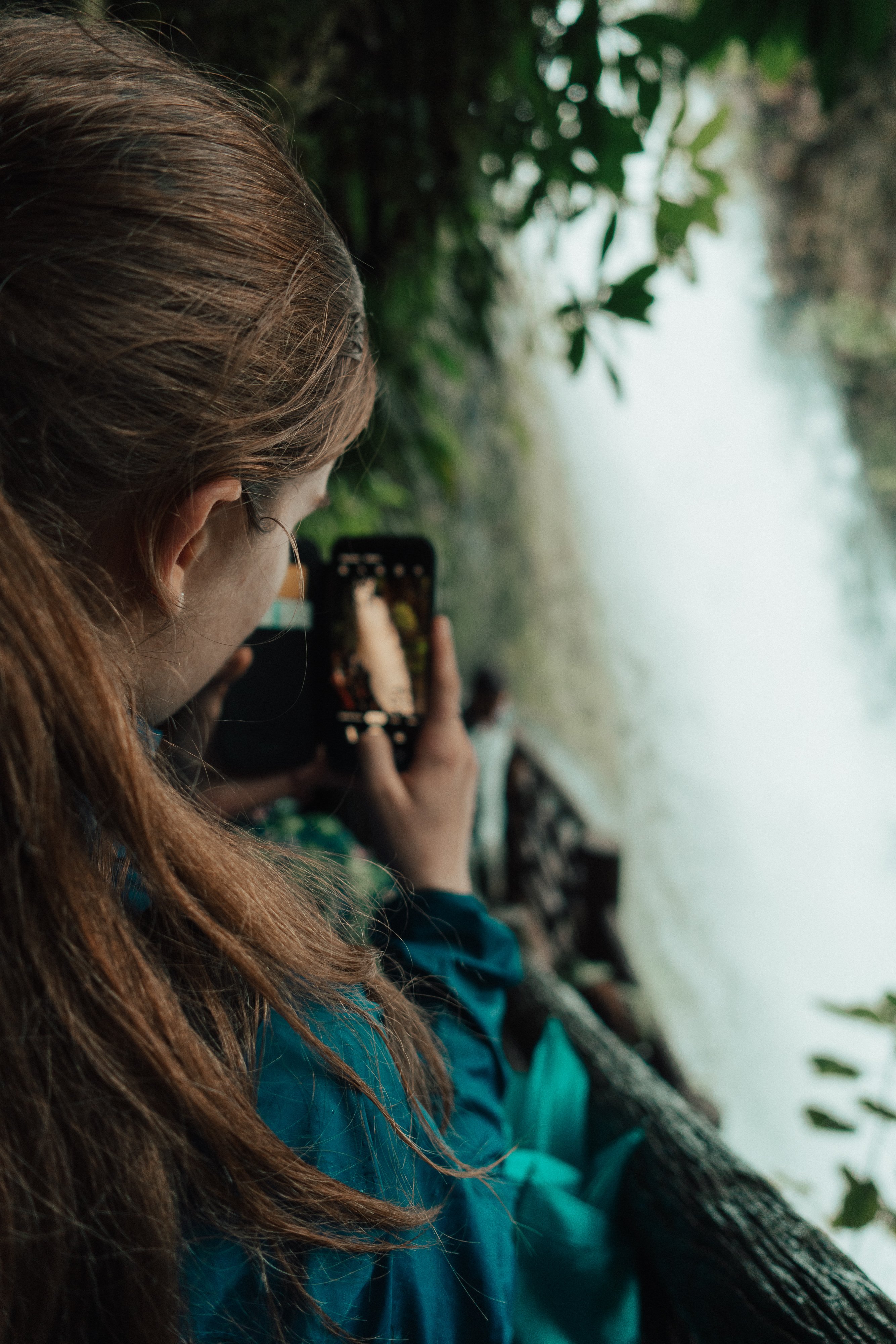 TrovaTrip woman in forest holding cellphone taking photo of waterfall