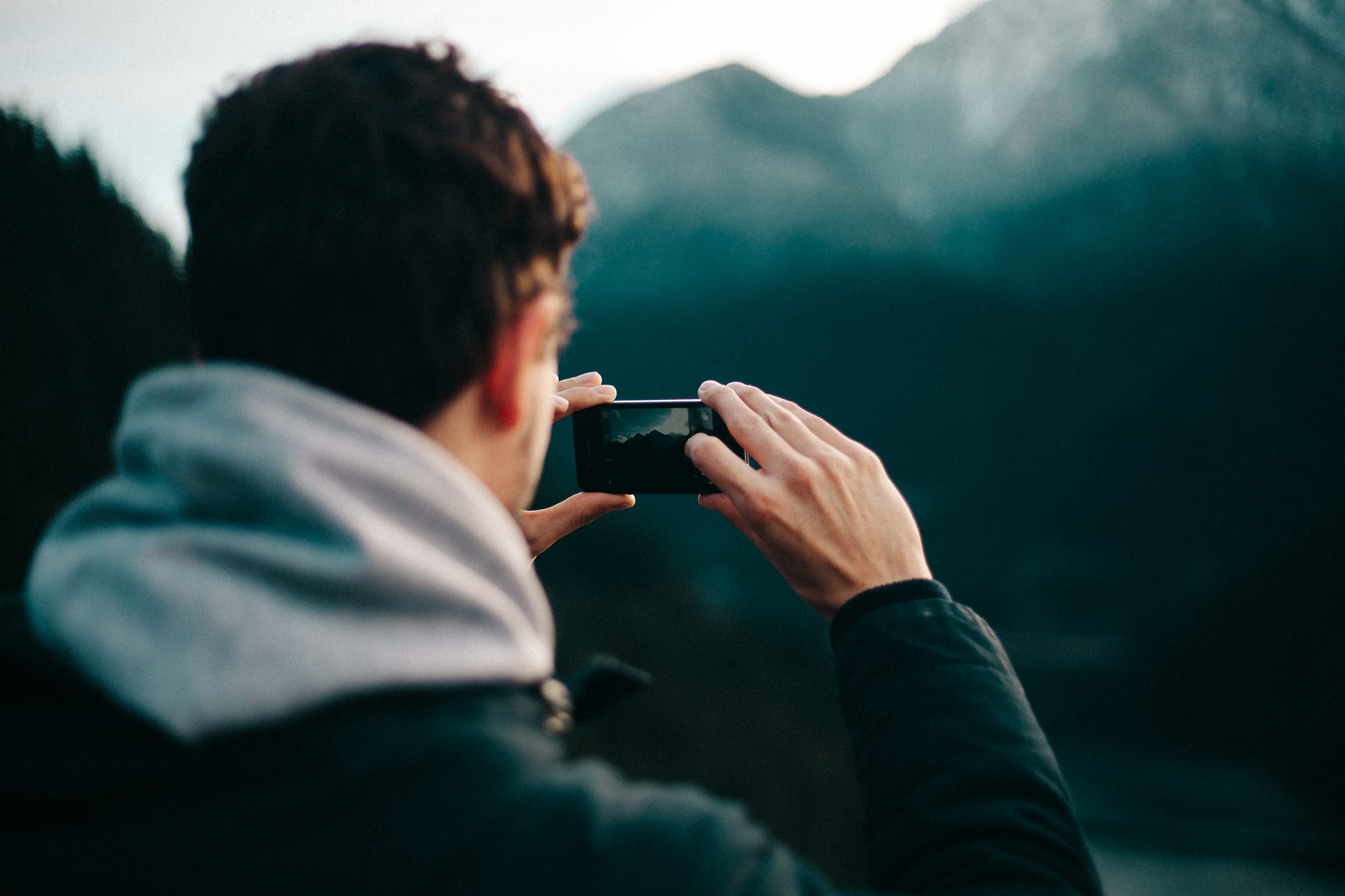 TrovaTrip man holding phone horizontally taking a picture of the large mountain in front of him