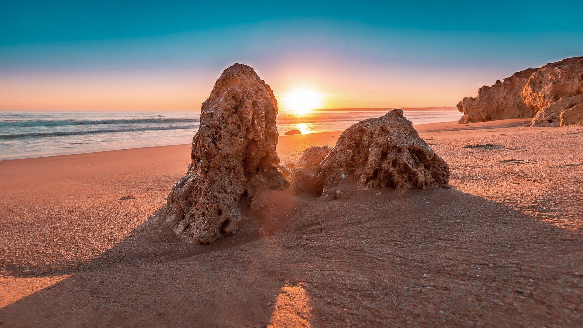 TrovaTrip rock formation on the shores of a beach with sun setting behind the horizon in Portugal