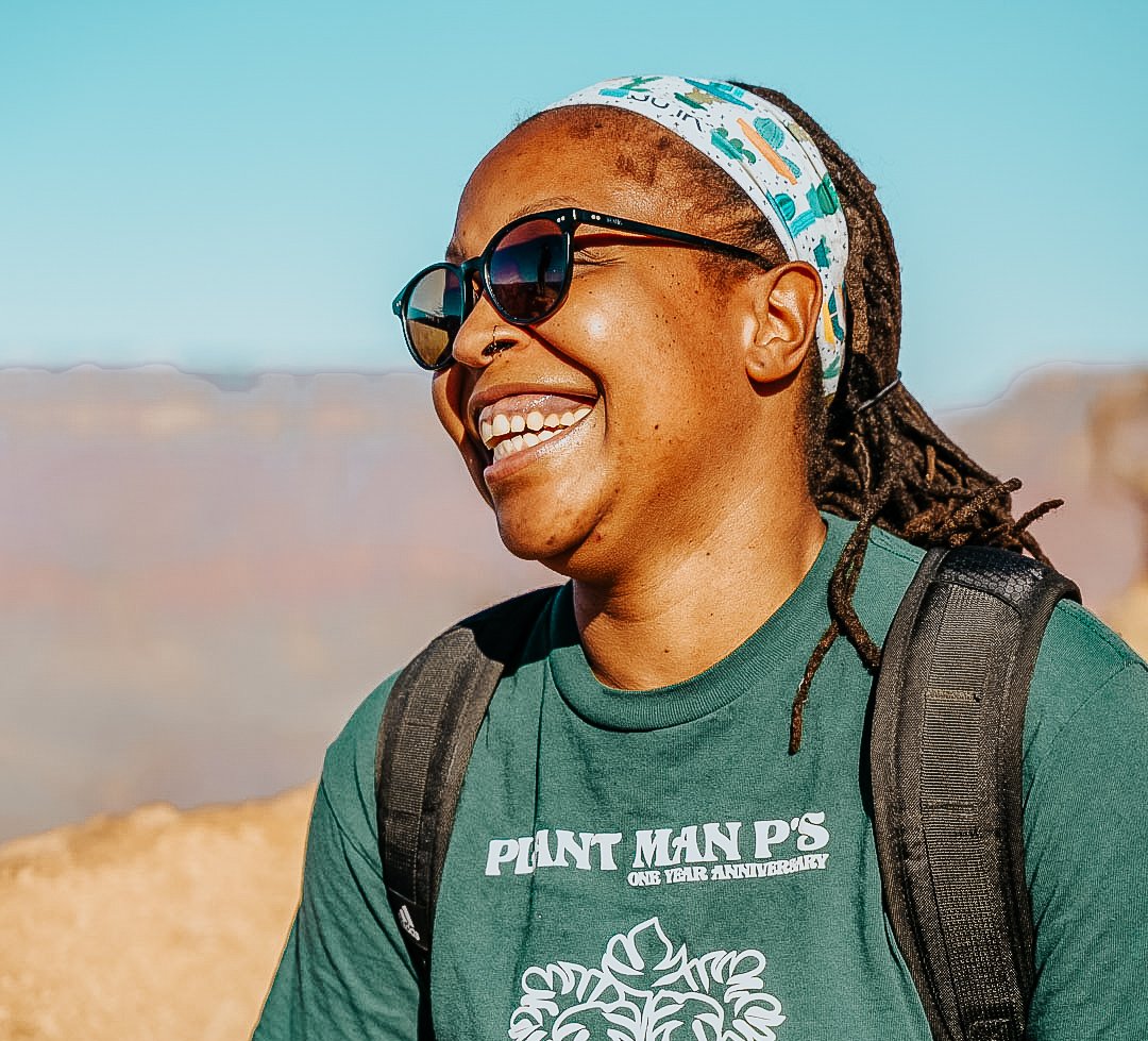 TrovaTrip woman smiling in a green shirt with a backpack and sunglasses in Zion