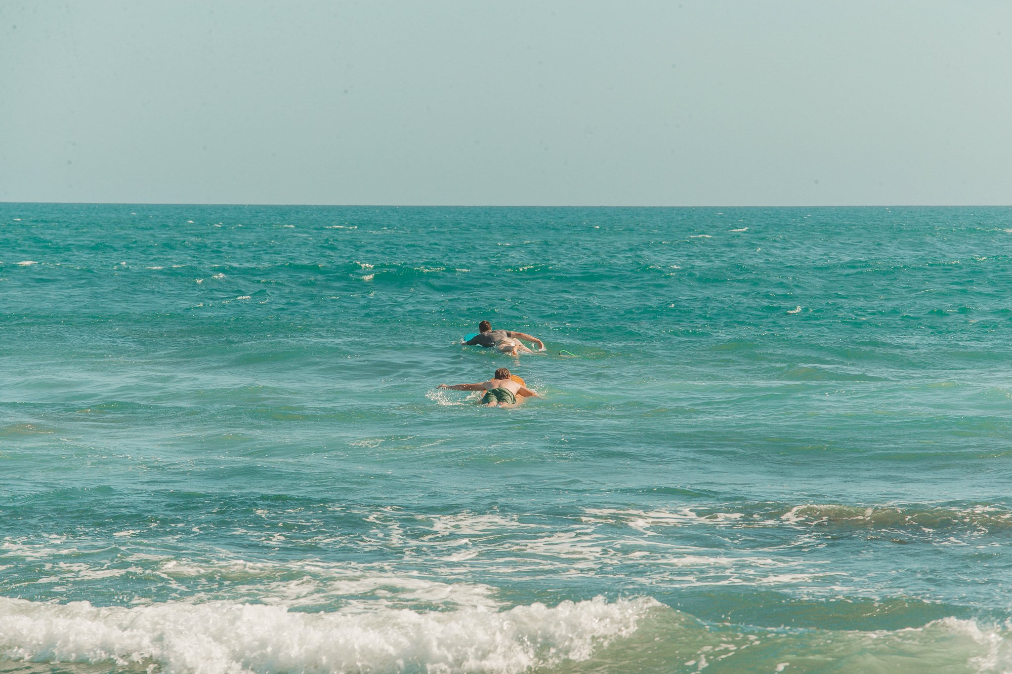 TrovaTrip two people in the clear blue water laying on surf boards in Canggu 