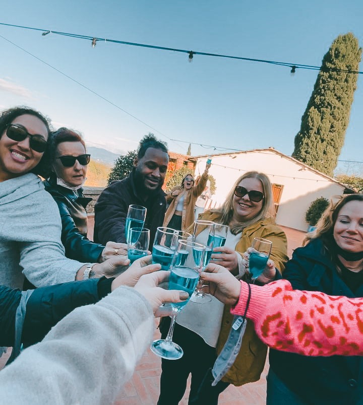 TrovaTrip group of travelers holding wine glasses full of blue liquid in a circle and celebrating with a cheers in Italy