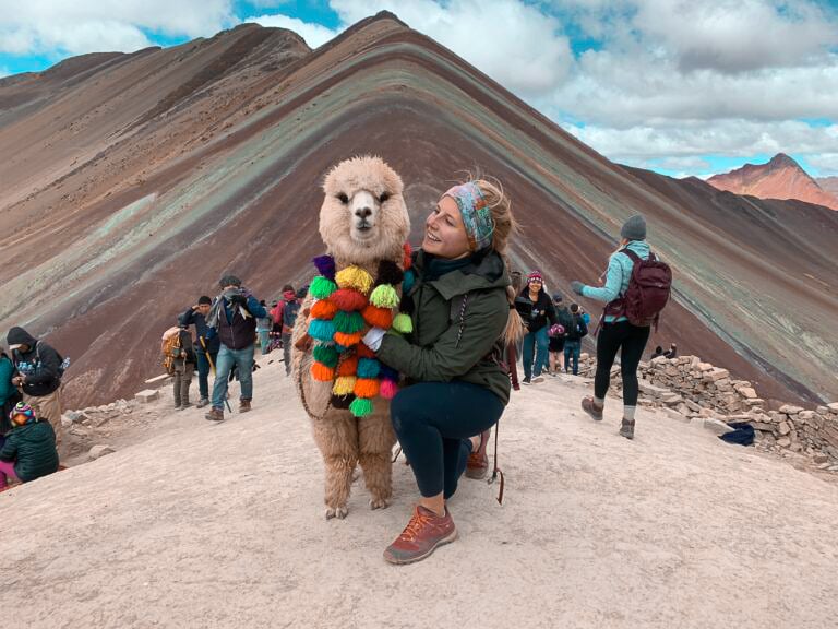 TrovaTrip traveler smiling next to llama or alpaca on painted rainbow mountains in Peru