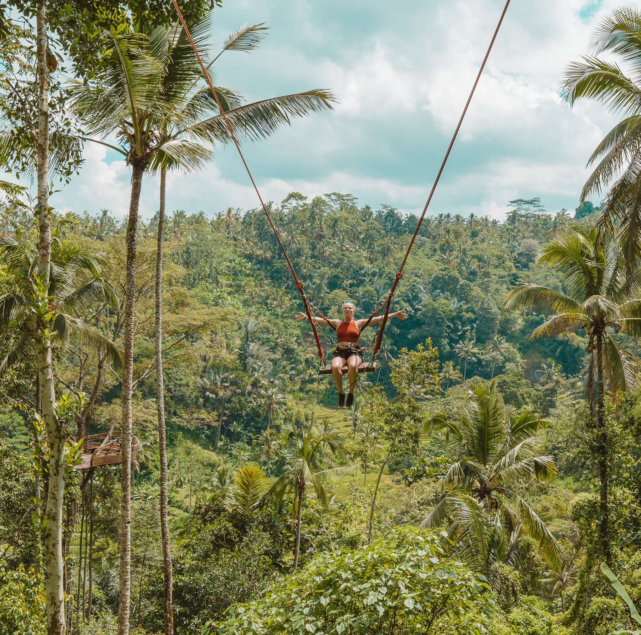TrovaTrip woman sitting on a swing elevated above the forest with her arms outstretched in Ubud