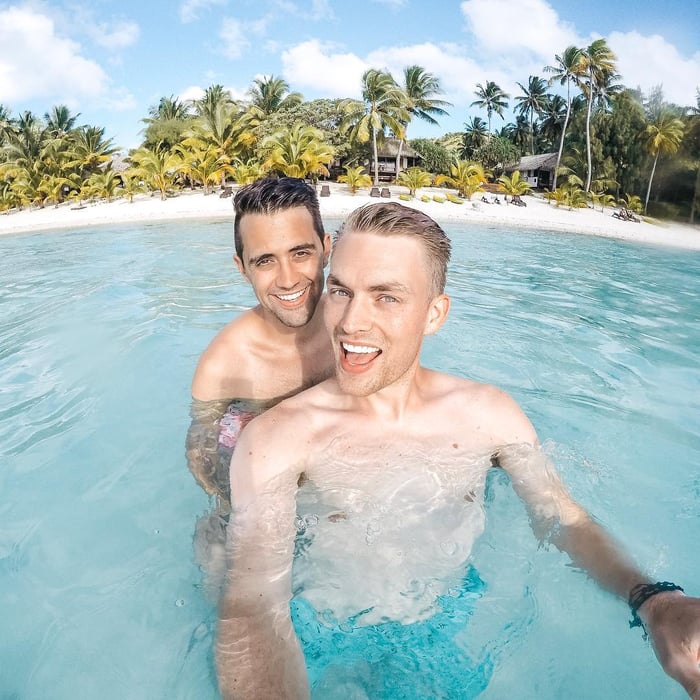 TrovaTrip two travelers smiling in ocean waters with shore behind them