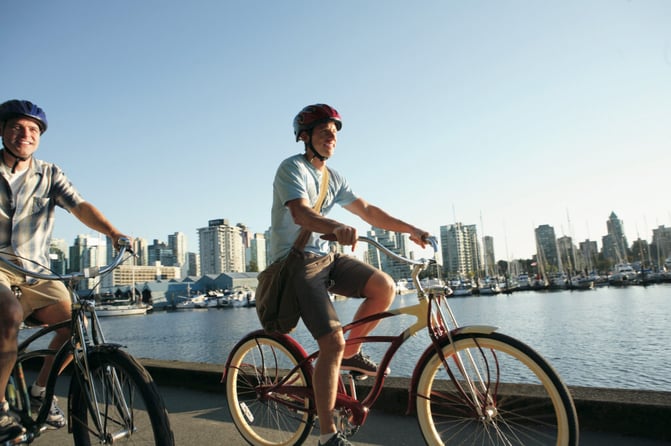 TrovaTrip two people riding bikes in a city with a river to their left full of boats