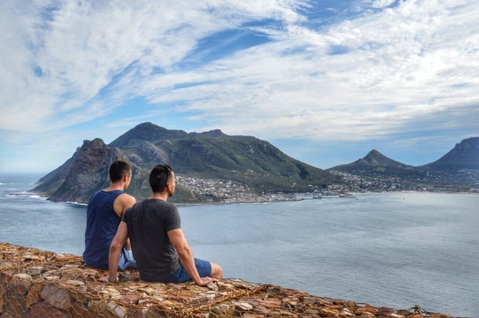 TrovaTrip two men sitting on a ledge of rocks looking out at the water and island in front of them