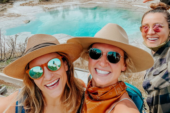 TrovaTrip Yellowstone women in hats and sunglasses smiling in front of geothermal pool