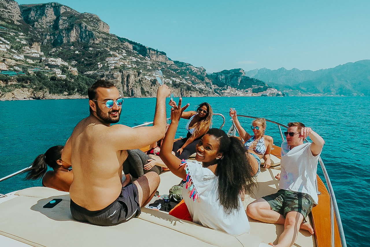 TrovaTrip group of travelers looking behind them with smiles on a boat with blue waters in Italy