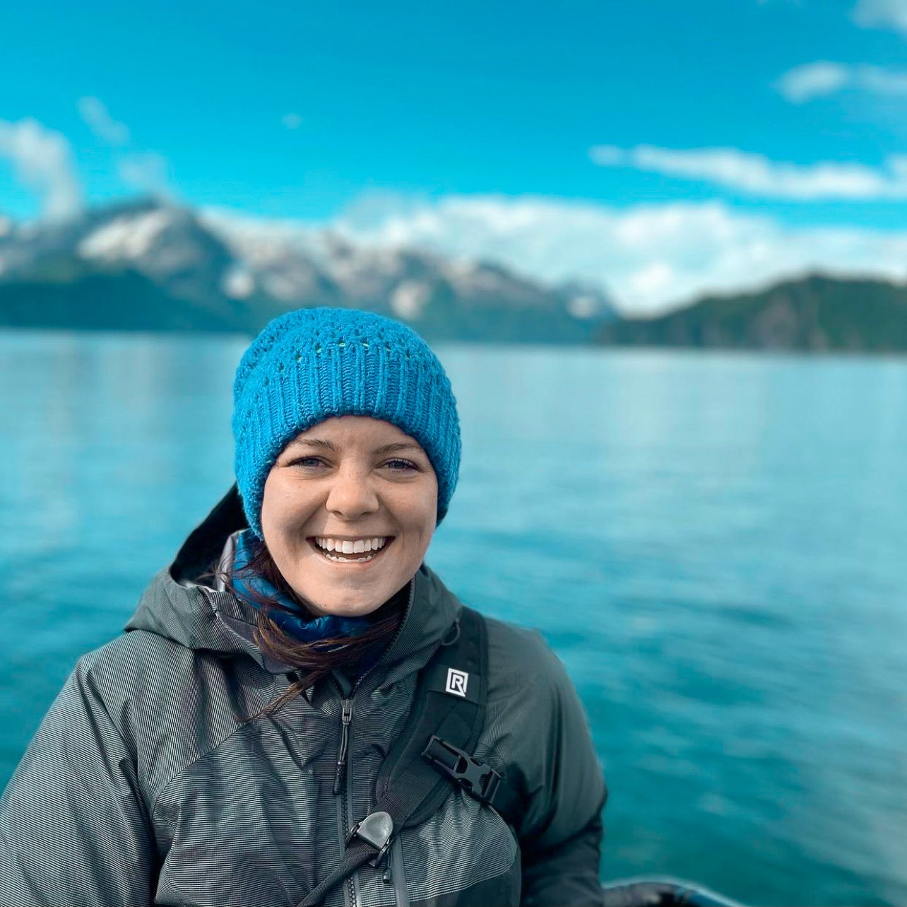 TrovaTrip traveler smiling at camera in blue hate and blue ocean behind her