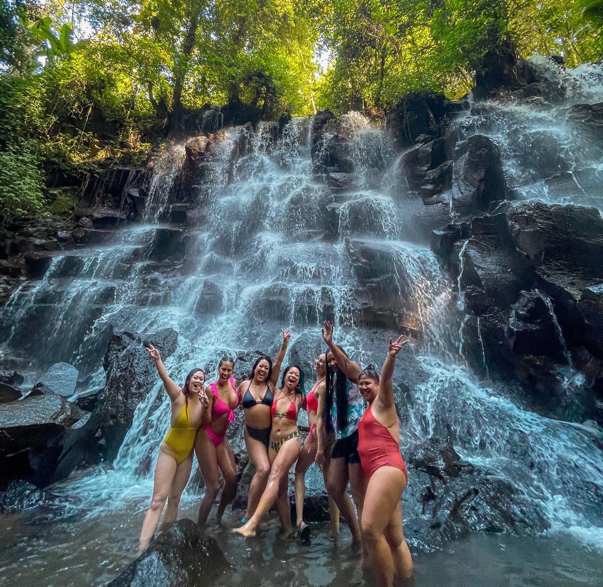 TrovaTrip Host @withrubina and travelers in Bali under waterfall.
