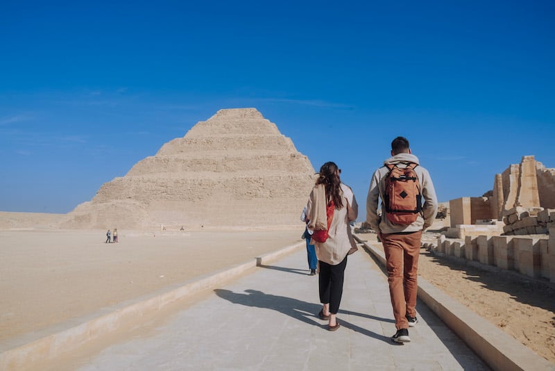 Two Travelers walking toward a pyramid on a TrovaTrip to Egypt with Hosts @dlarock and @cassandrayahniane.