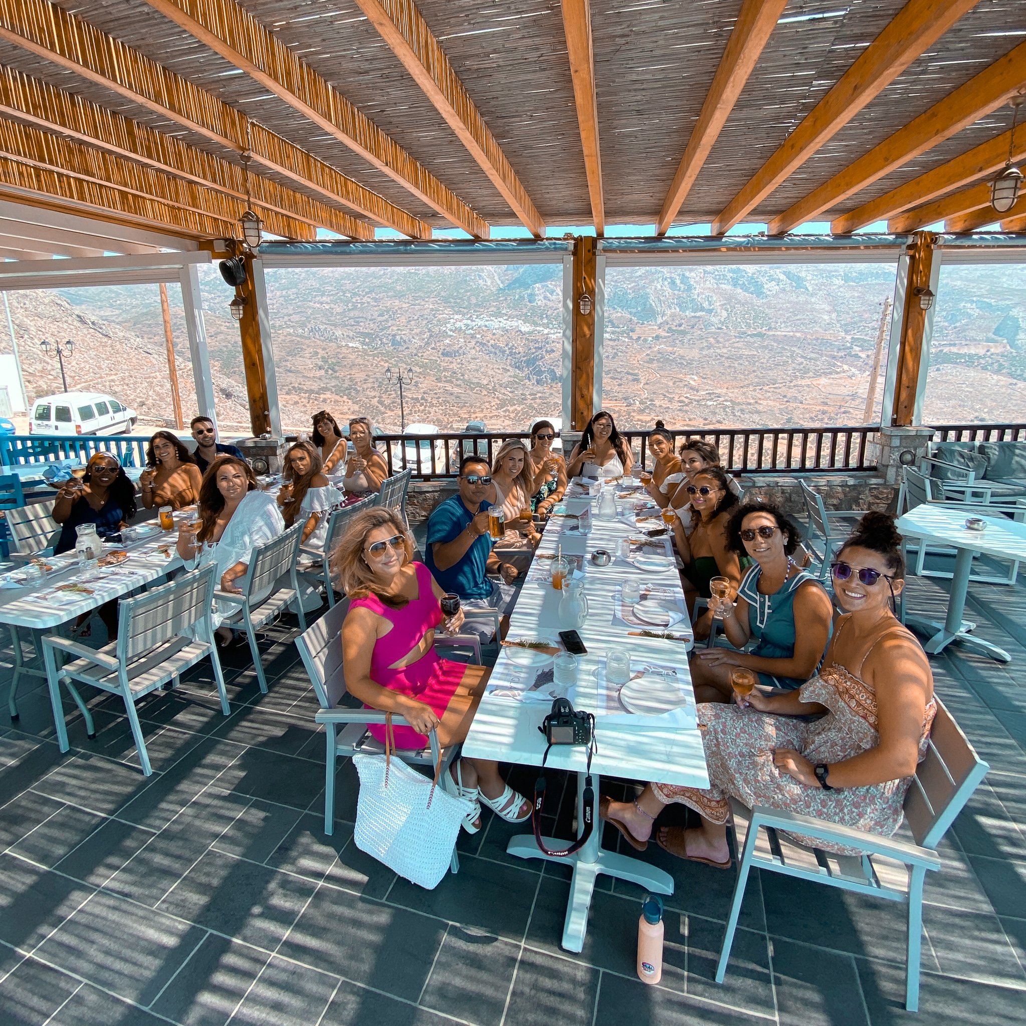 TrovaTrip travelers sitting at two large white tables dining in Greece with mountains in the background
