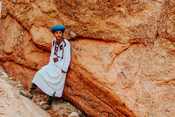 TrovaTrip Man in Morocco leaning against a mountain in traditional headdress and smock
