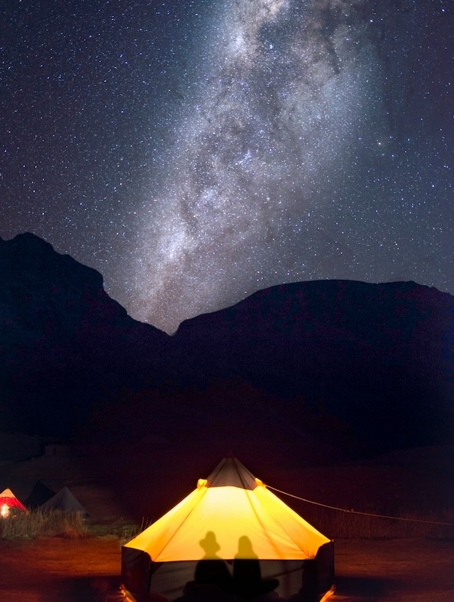 A tent lit up inside below a starry night sky.